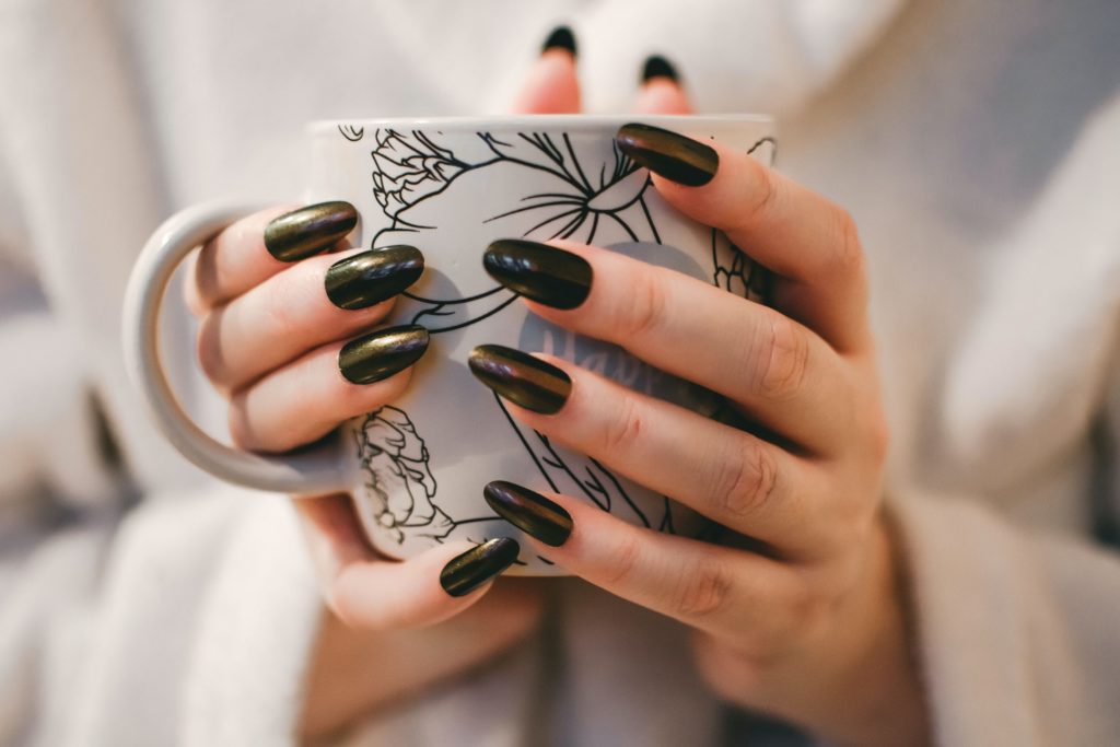 Woman with painted black nails holding a flowery mug with the words happy on
